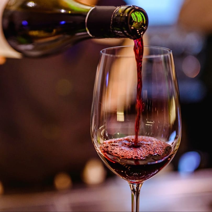 Red wine pouring from a bottle into a clear wine glass, creating foamy bubbles.