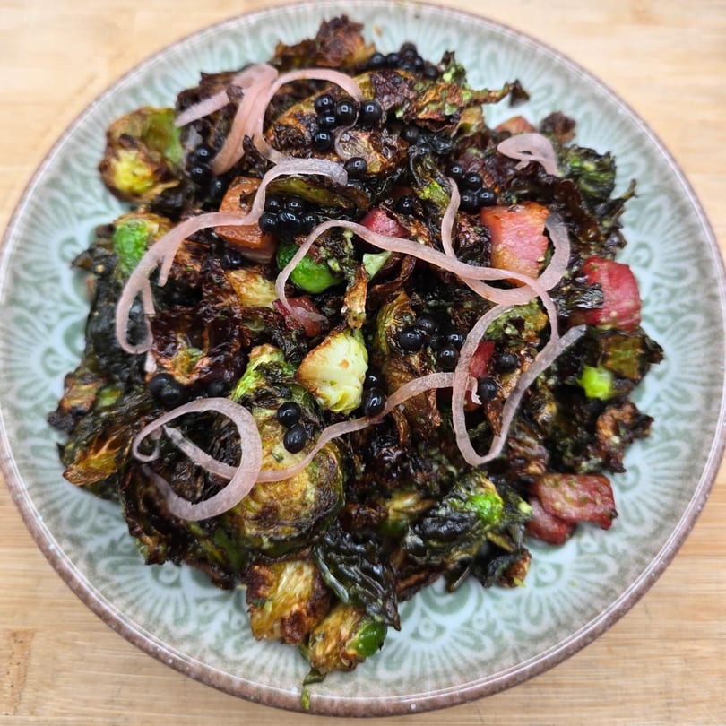 Crispy Brussels sprouts with bacon, pickled red onions, and black caviar on a patterned plate.