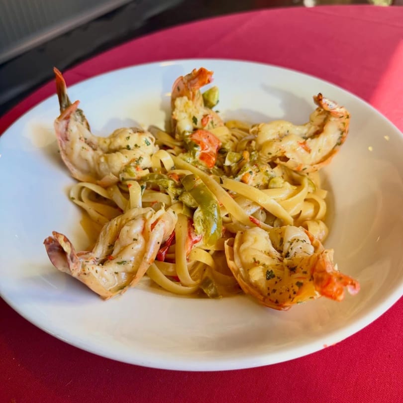 Shrimp scampi with fettuccine pasta, green peppers, and red peppers on a white plate.