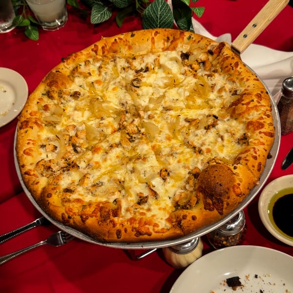A large, cheesy chicken and onion pizza on a metal tray, with a red tablecloth background.
