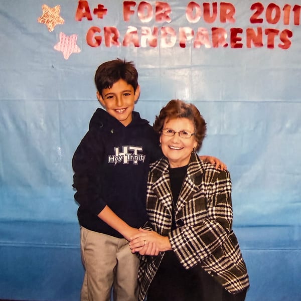 A young boy and an older woman smiling, holding hands, with a blue background and red text.