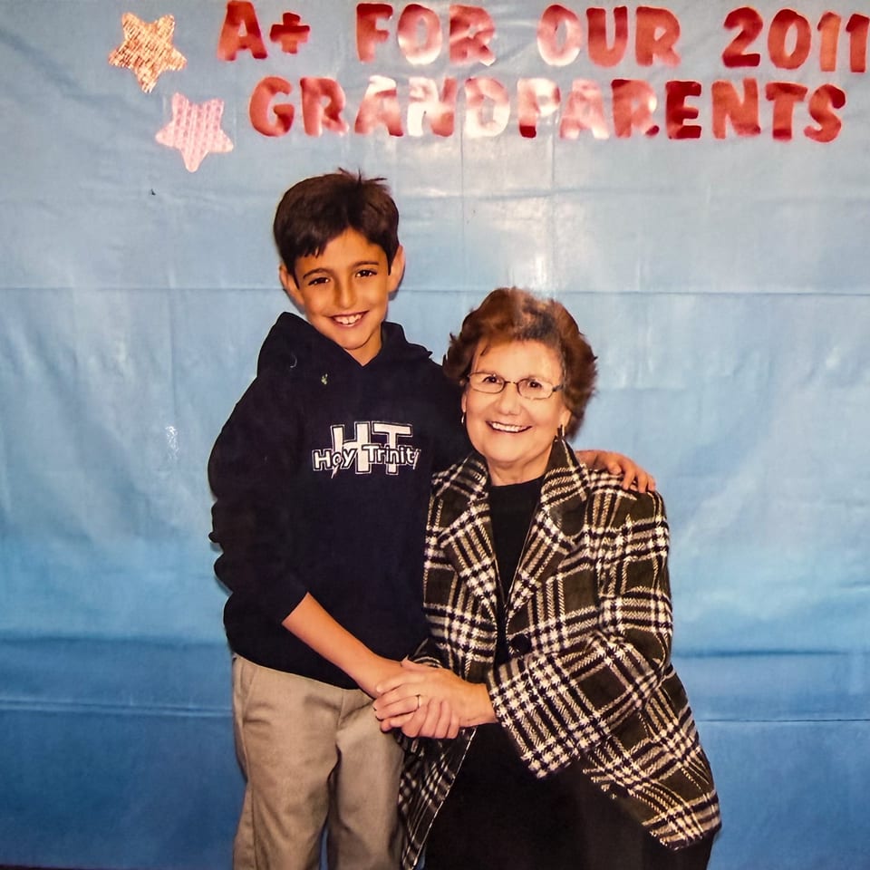 A young boy and an older woman smiling, holding hands, with a blue background and red text.