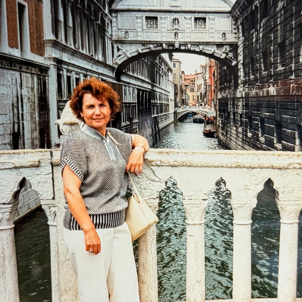 Woman with red hair leaning on a stone bridge railing overlooking a Venetian canal.