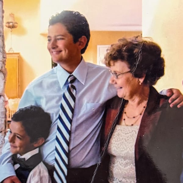 Three generations of a family, a young boy, a man, and an older woman, smiling together.