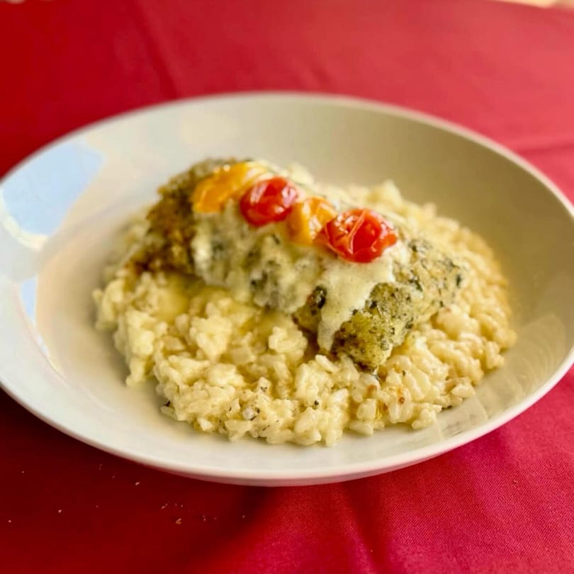 Chicken with melted cheese and cherry tomatoes on a bed of risotto, served on a white plate.