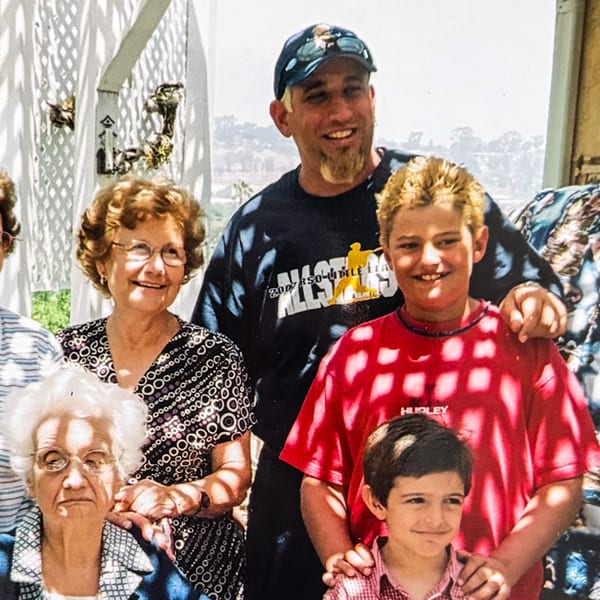 A family of five, three generations, smiling for a photo outdoors on a sunny day.